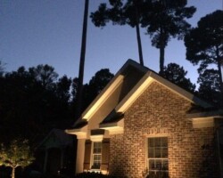 Beautifully illuminated Bluffton brick home with outdoor lighting and surrounded by trees. Elegant exterior lighting highlights the architecture of the brick house at night in Bluffton, SC.