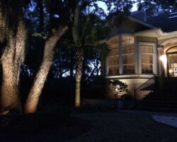 Garden and house exterior on Hilton Head illuminated with professional outdoor lighting, creating inviting ambiance. Beautifully lit Hilton Head Home with landscape lighting highlighting trees and exterior features.