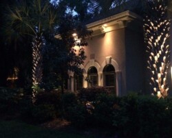 Illuminated house exterior at dusk with strategic outdoor lighting under trees and on a home in the Hilton Head area. Elegant exterior house lighting highlighting palm trees and architecture in the Hilton Head area.