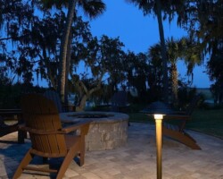 Enhance your outdoor space with warm lighting for relaxing evenings and added safety along the Hilton Head area's Broad River. Stylish outdoor lamp illuminating a patio area at dusk with trees and seating along the Broad River in the Hilton Head area.