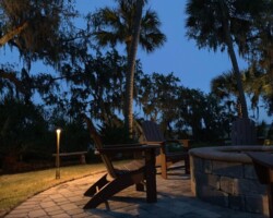 Enhance your Hilton Head area outdoor space with cozy lighting for relaxing evenings, featuring chairs, fire pit, and lush garden. Outdoor patio lighting along the waterfront with warm LED lamps highlighting seating and fire pit area at dusk in the Hilton Head coastal region.